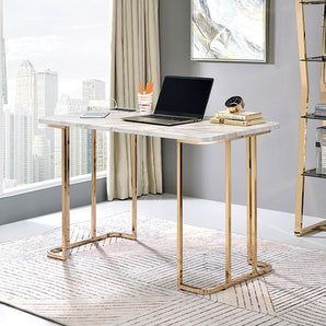 Delphine Faux Marble Top Desk in Gold/White. A plating process is used to finish the sturdy steel frame with a beautiful golden hue, while the faux marble tabletop is durable and easy to maintain. A built-in USB and power outlet plug allows for continued creativity and productivity in the convenience of your own home office.